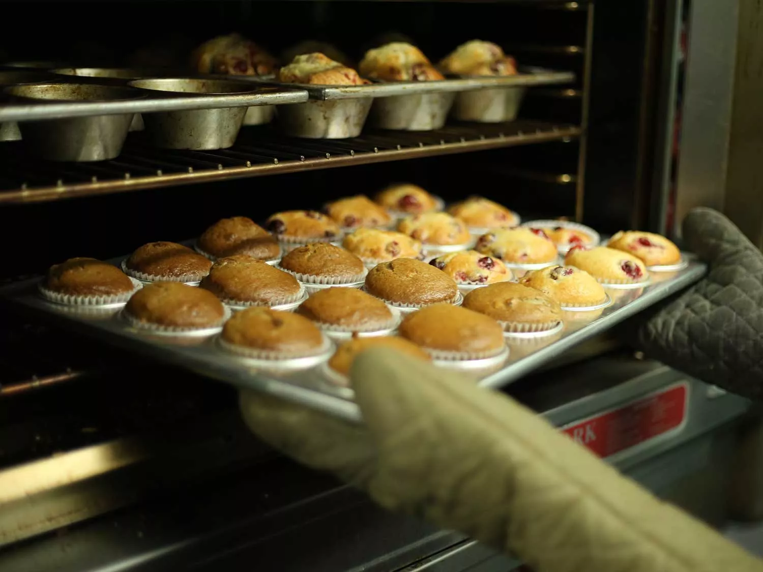 Taking out muffins with oven mitts.