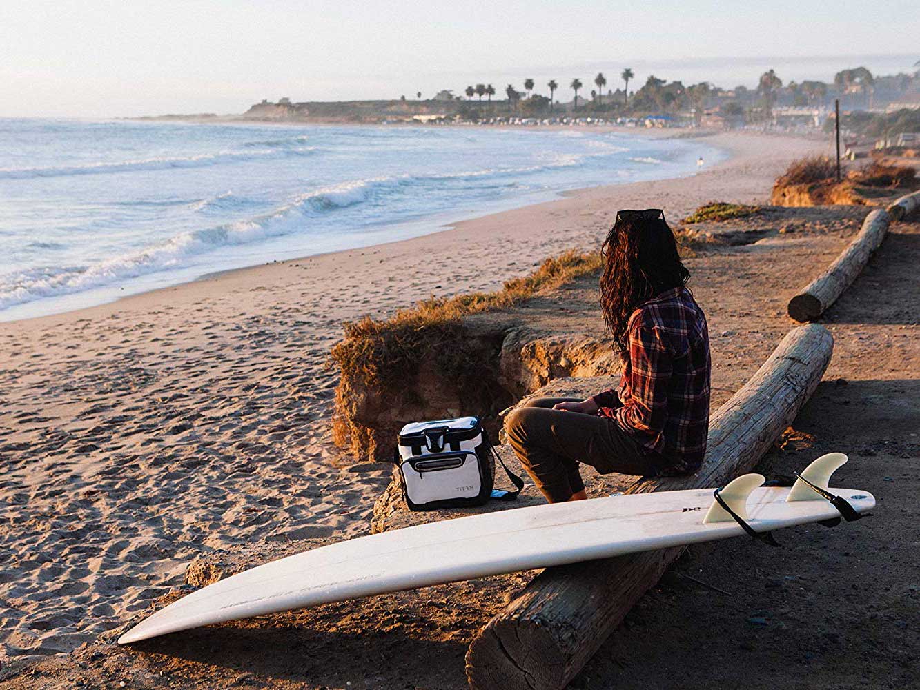 Woman carries small insulated cooler to beach.