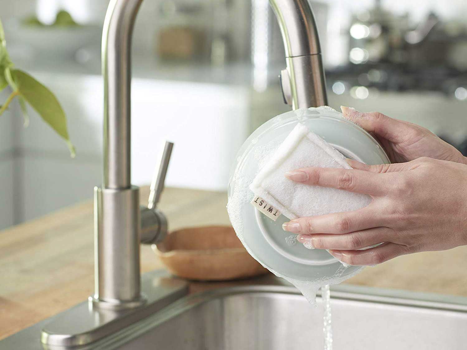 Washing dishes under soapy water with sponge.