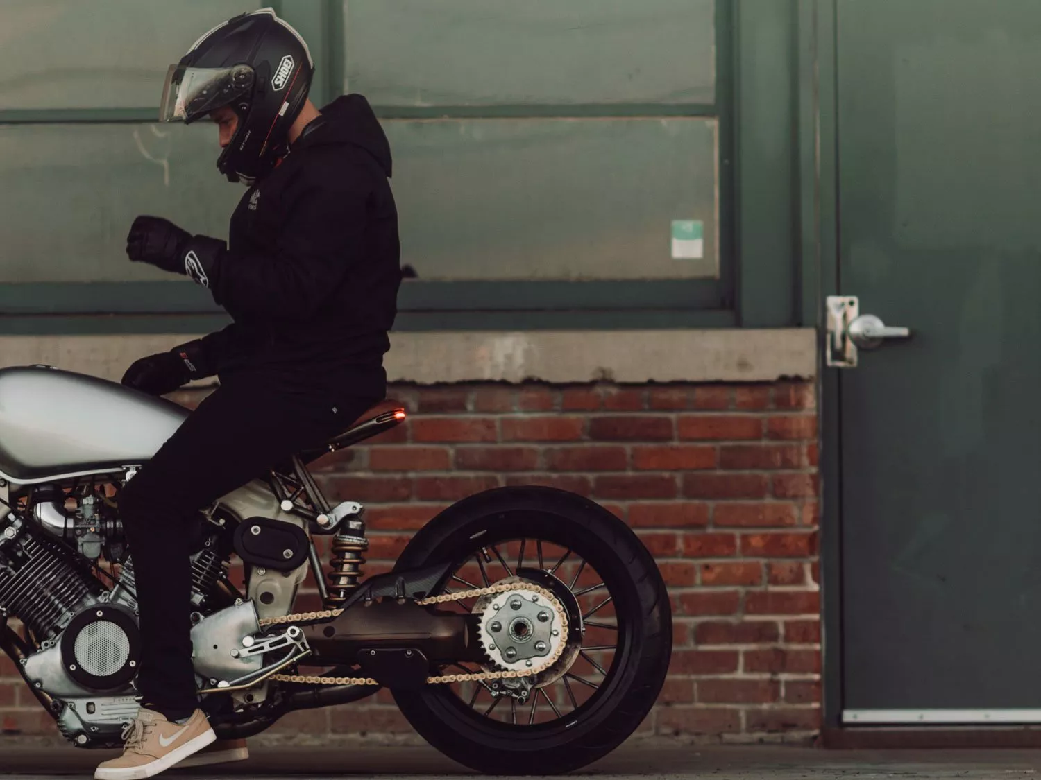 Motorcyclist sitting on motorcycle with drive chain lubed up.