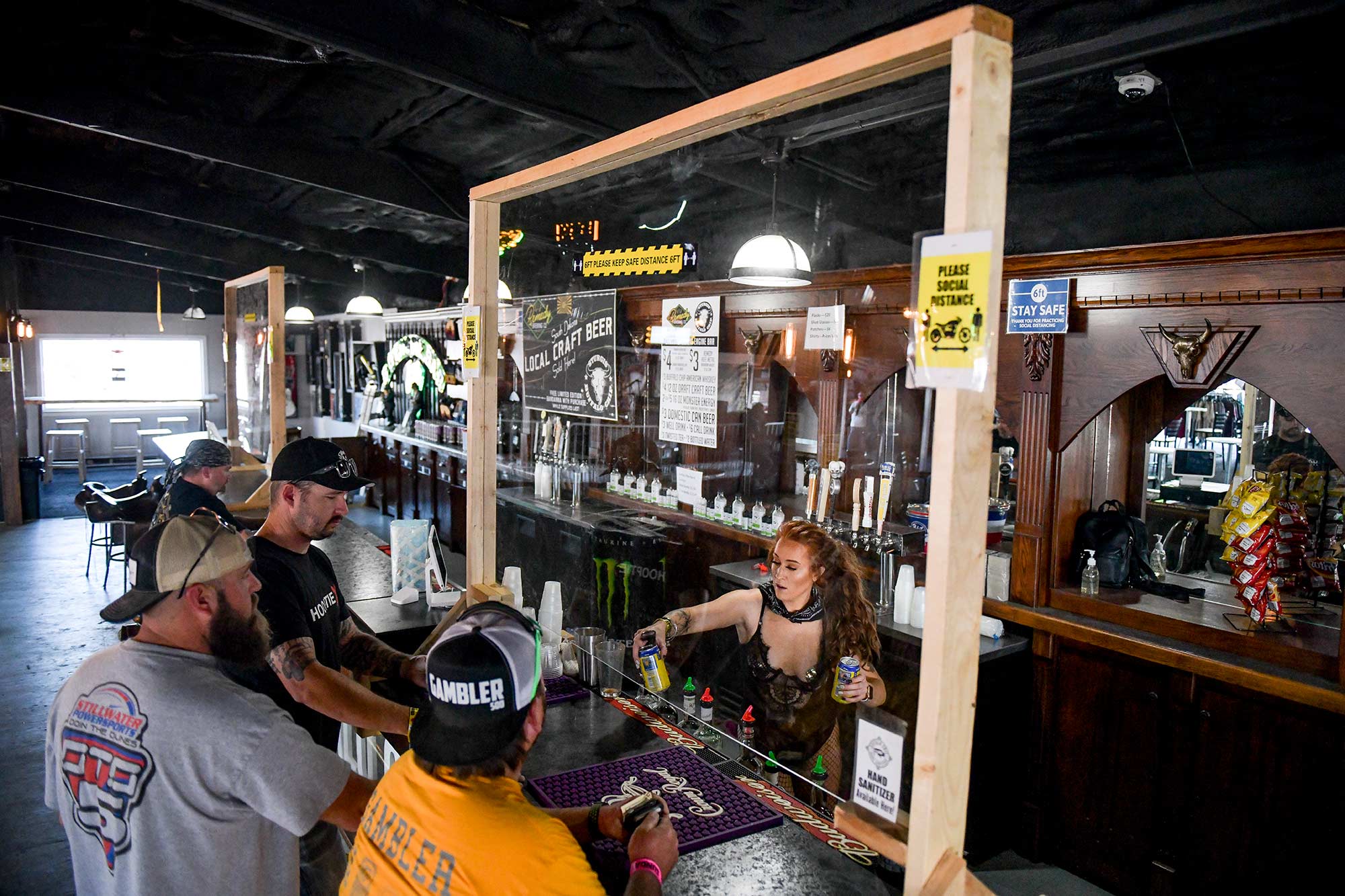 A bartender serves drinks from behind a plexiglass shield in Sturgis.